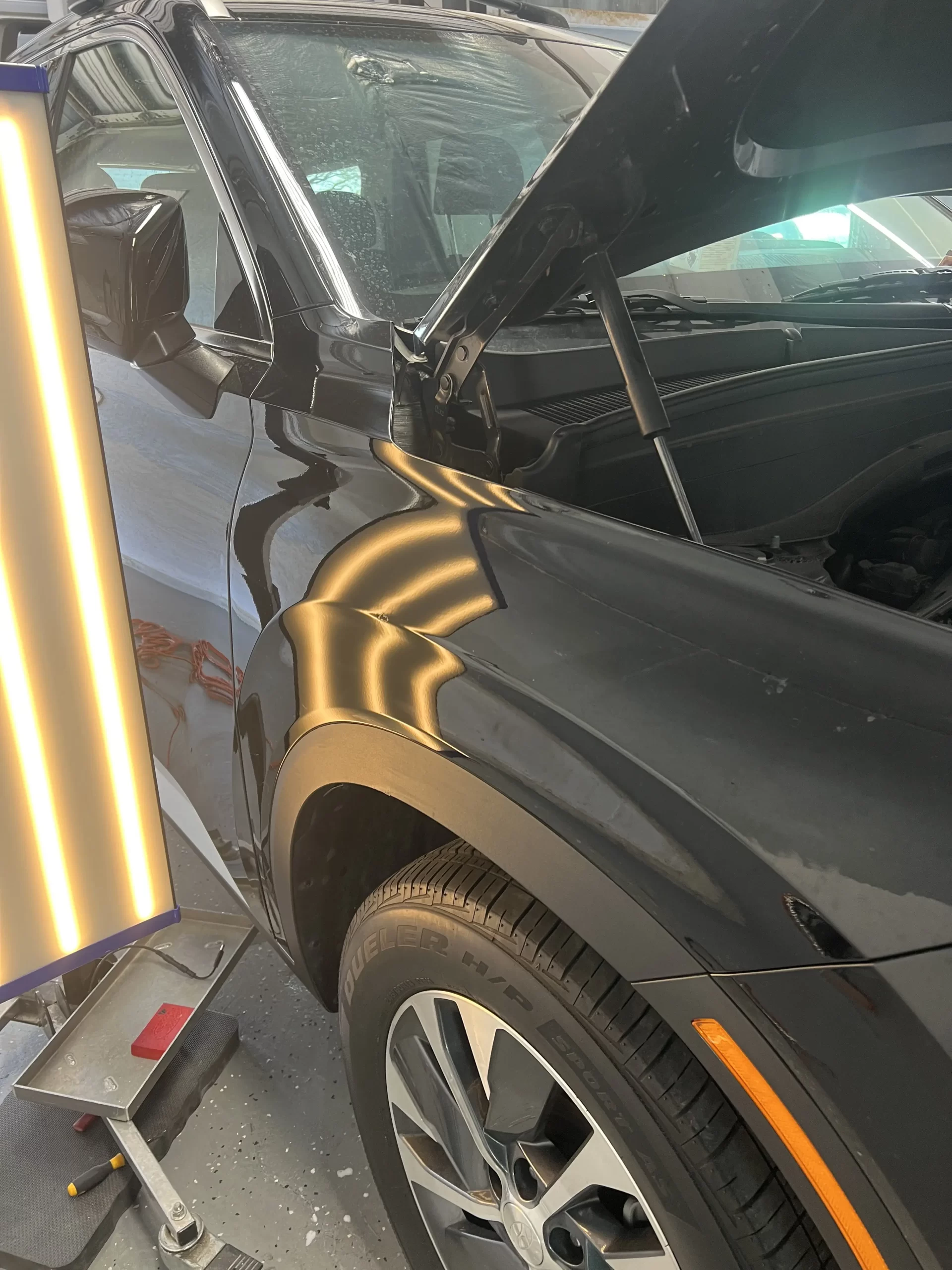 A black pickup with its hood open and illuminated after being serviced.