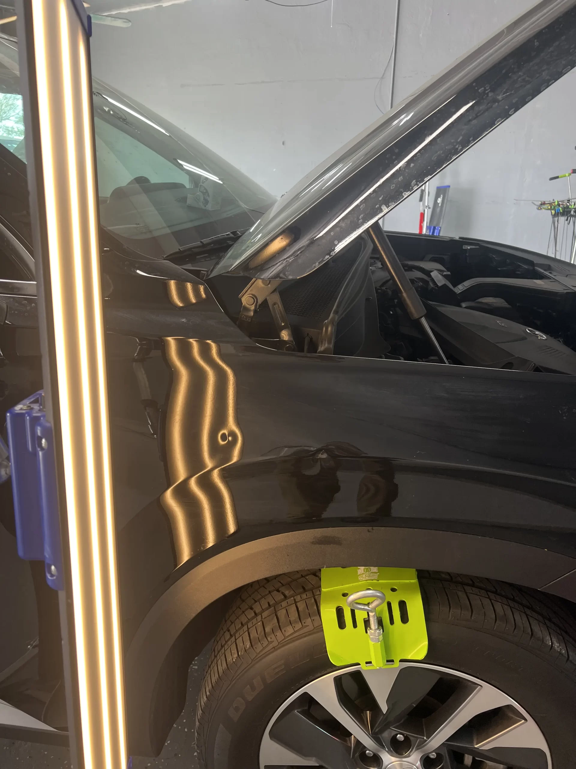 A black car inside an auto garage and its hood open for repair.