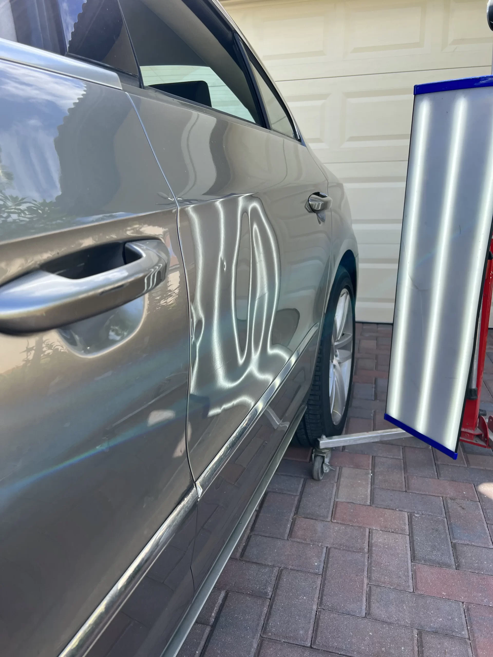 The slightly disfigured right side of a grey car door panel prior to being repaired.