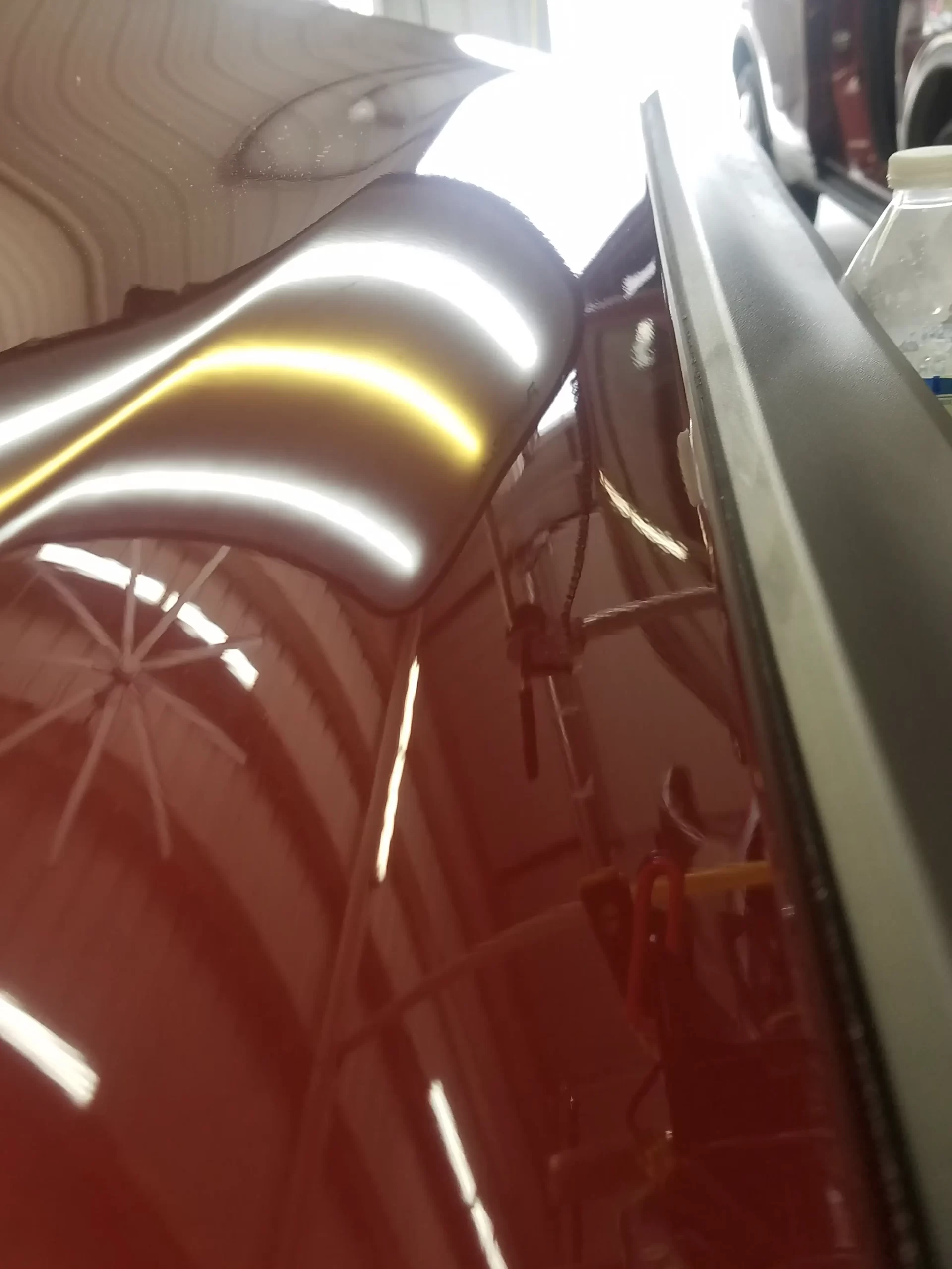 The shiny surface of a cherry red vehicle in a garage after repairs.