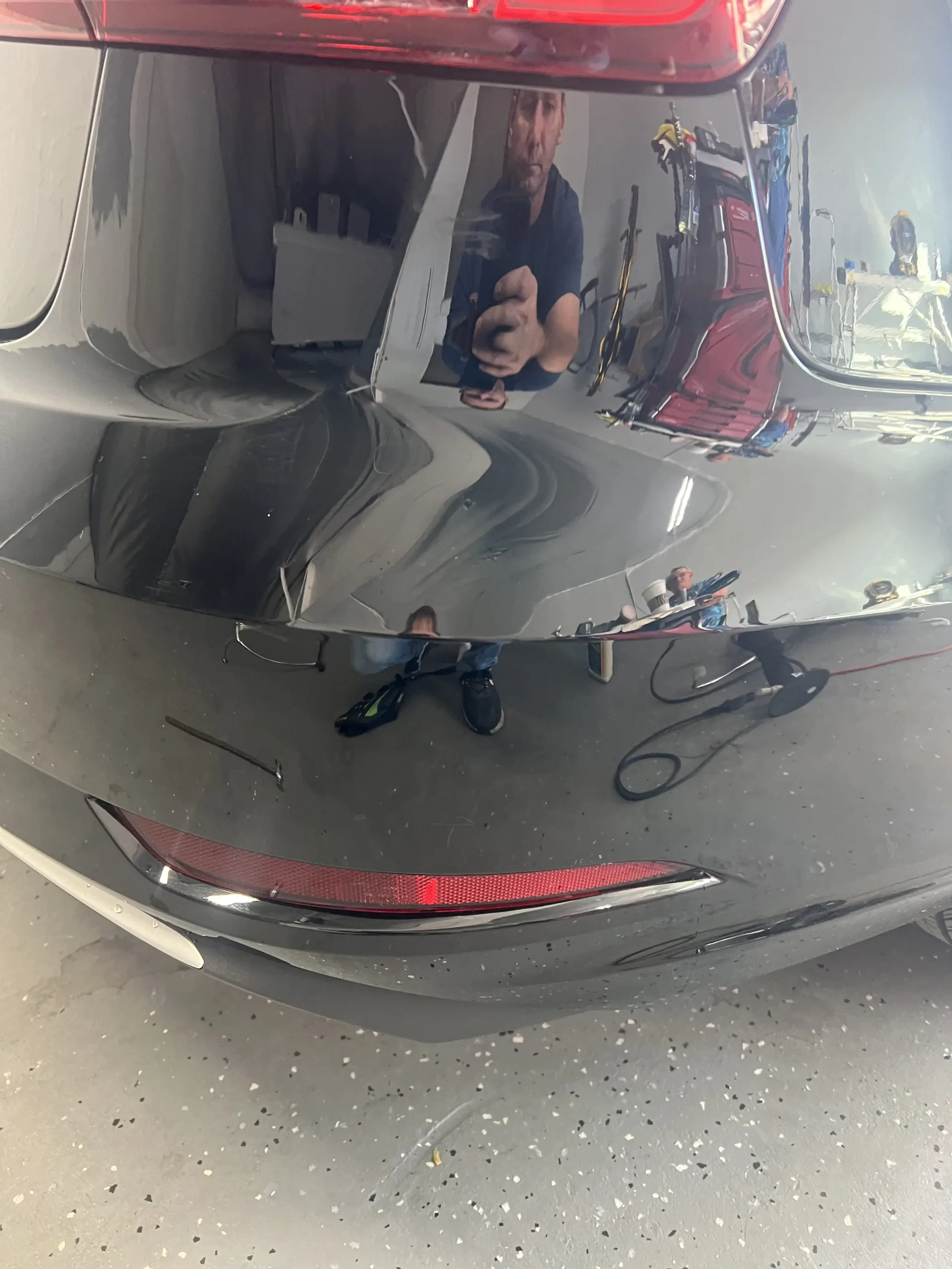 The back portion of a black vehicle with a reflection of a man taking a picture of it after repairs were made.