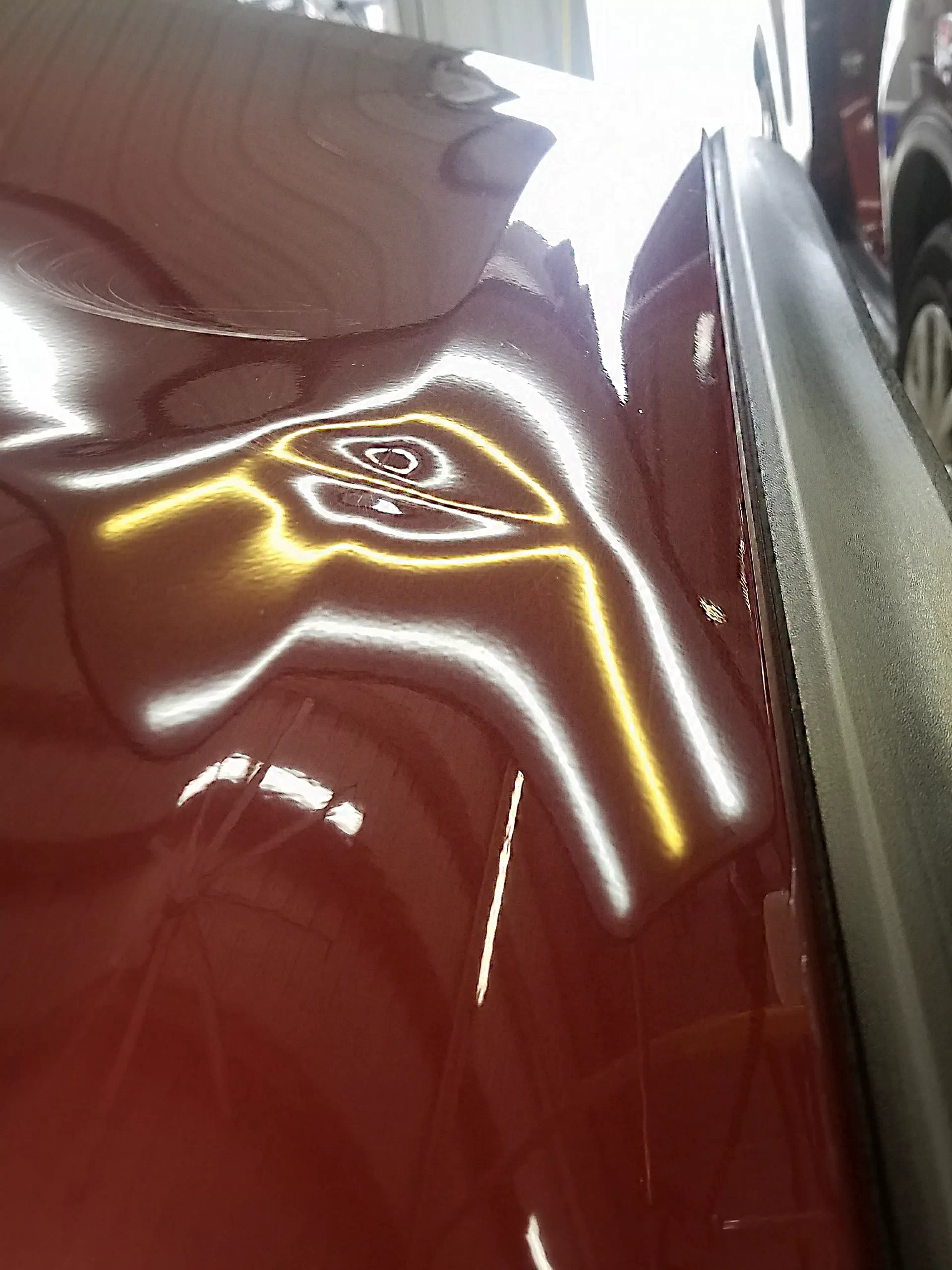 The slightly dented surface of a cherry red vehicle before in a garage prior to repairs.
