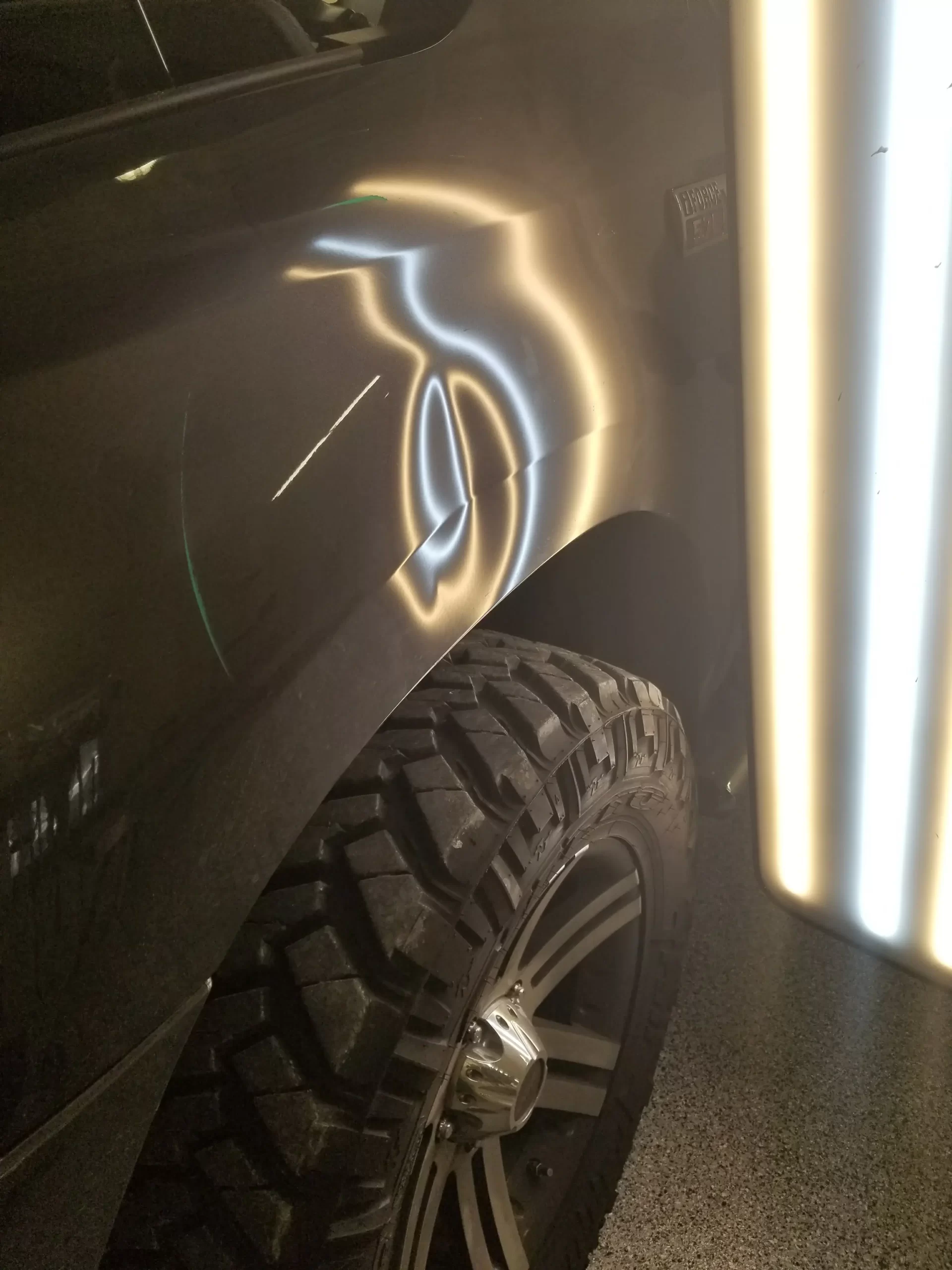 The side of a slightly dented grey pickup truck is lit up prior to repairs.