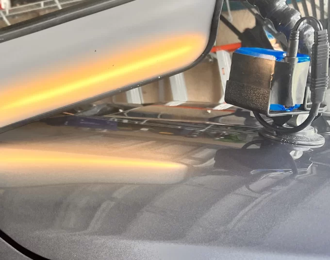The hood of a black vehicle with a reflective device attached to it.